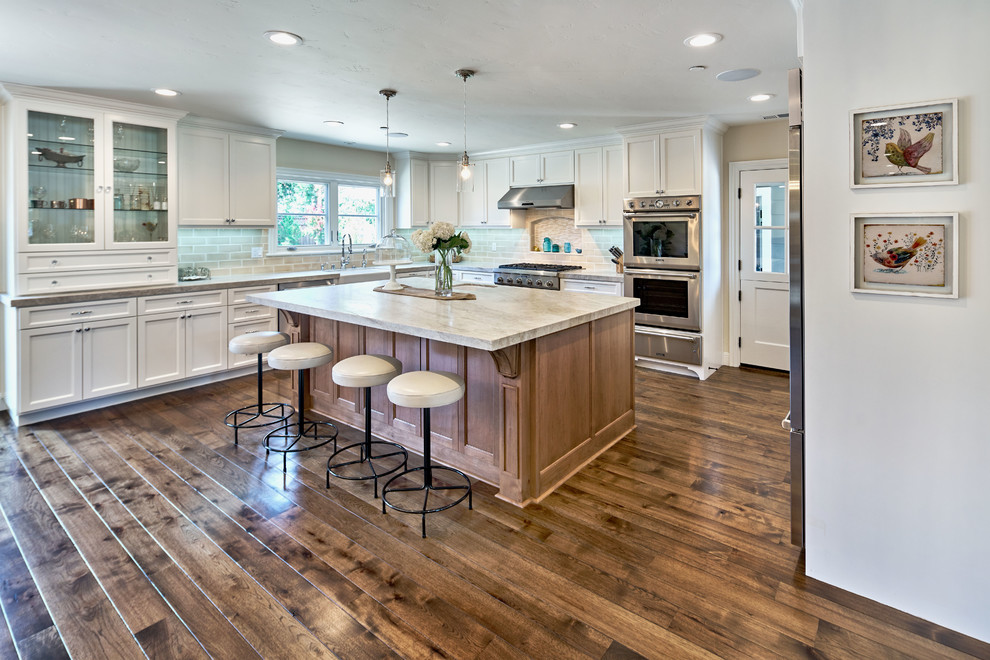 Large traditional l-shaped open plan kitchen in San Francisco with a farmhouse sink, shaker cabinets, white cabinets, quartzite benchtops, white splashback, subway tile splashback, stainless steel appliances, dark hardwood floors and with island.