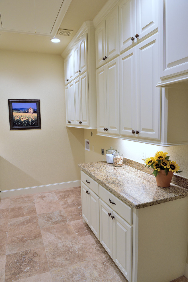 Photo of a large mediterranean galley dedicated laundry room in Houston with an undermount sink, white cabinets, granite benchtops, beige walls, travertine floors, a side-by-side washer and dryer and beige floor.