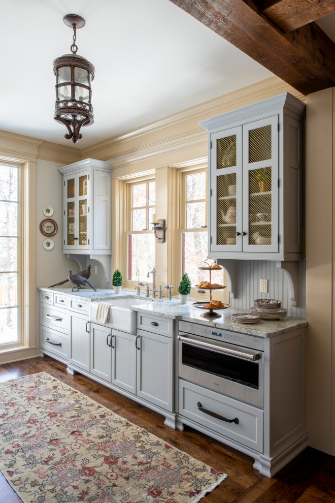 Inspiration for a large l-shaped kitchen pantry in Minneapolis with a farmhouse sink, recessed-panel cabinets, blue cabinets, granite benchtops, beige splashback, ceramic splashback, stainless steel appliances, medium hardwood floors, with island, brown floor, beige benchtop and exposed beam.