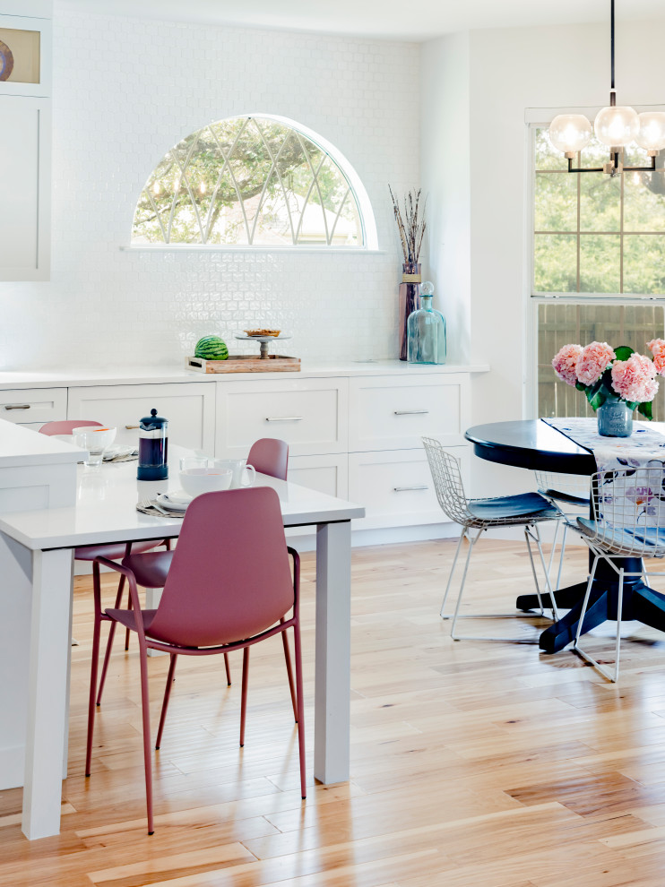 Large transitional l-shaped light wood floor and brown floor eat-in kitchen photo in Austin with a single-bowl sink, shaker cabinets, white cabinets, quartz countertops, white backsplash, ceramic backsplash, stainless steel appliances, an island and white countertops