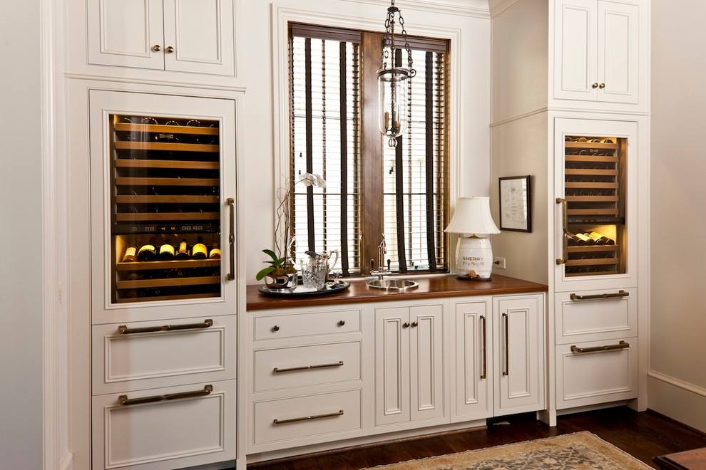 Photo of a traditional single-wall wet bar in Birmingham with a drop-in sink, beaded inset cabinets, wood benchtops, dark hardwood floors, white cabinets and brown benchtop.