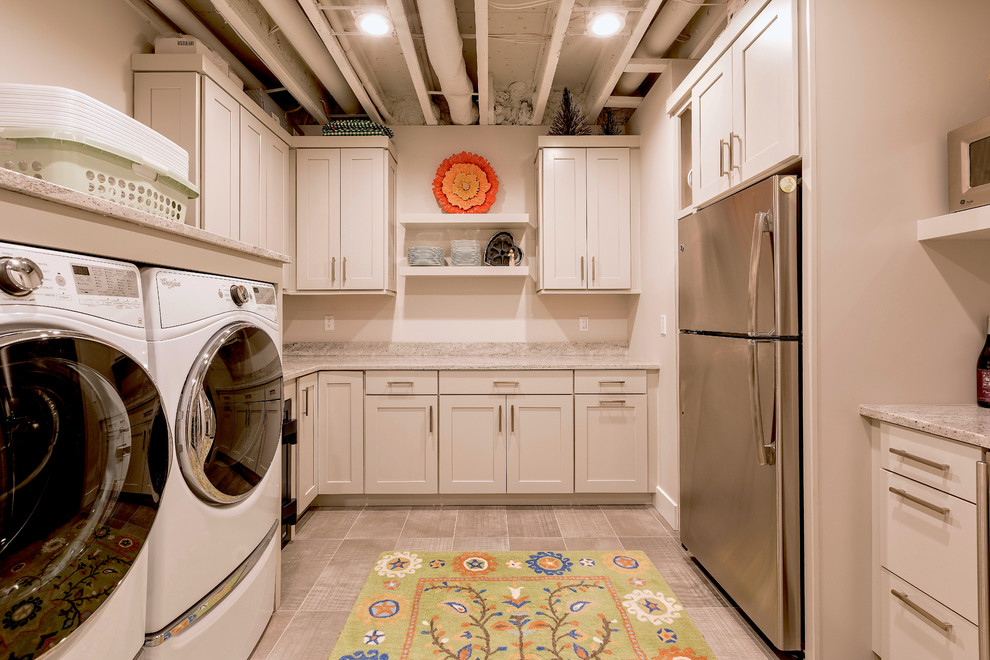 Photo of a small arts and crafts u-shaped utility room in Detroit with an utility sink, shaker cabinets, grey cabinets, granite benchtops, beige walls, porcelain floors, a side-by-side washer and dryer, grey floor and beige benchtop.
