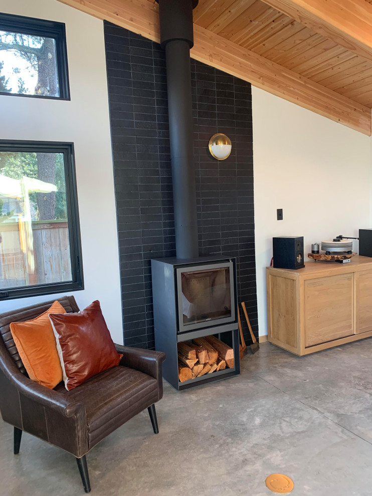 Mid-sized mid-century modern concrete floor, wood ceiling and brick wall family room photo in Portland with a wood stove and a brick fireplace
