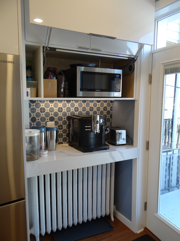 This is an example of a small modern galley separate kitchen in DC Metro with an undermount sink, flat-panel cabinets, white cabinets, quartz benchtops, blue splashback, cement tile splashback, stainless steel appliances, medium hardwood floors, a peninsula, orange floor and white benchtop.