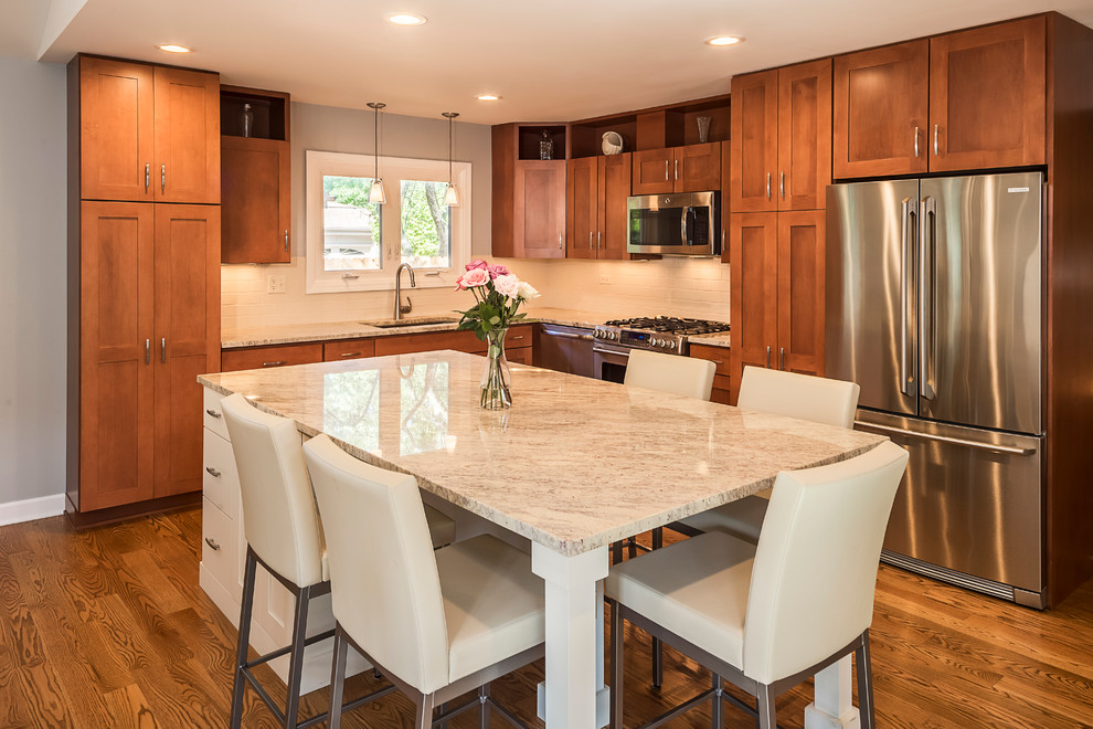 Mid-sized transitional u-shaped light wood floor eat-in kitchen photo in Chicago with a drop-in sink, recessed-panel cabinets, white cabinets, marble countertops, white backsplash, subway tile backsplash, stainless steel appliances and an island