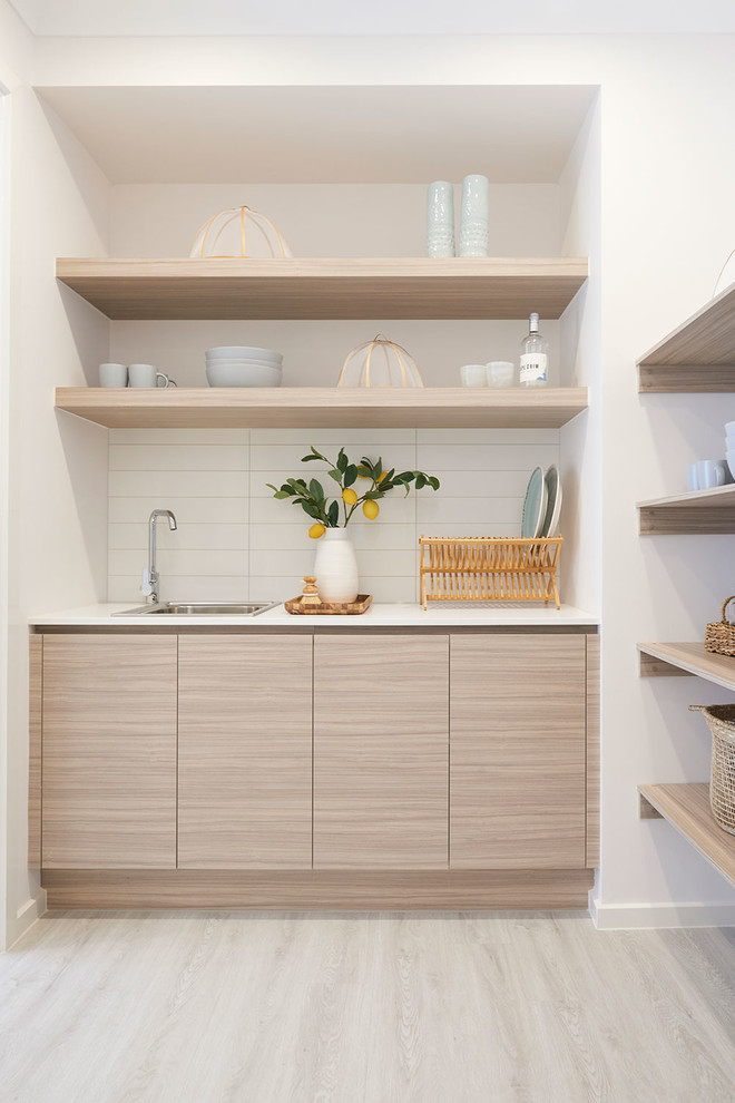 Photo of a beach style galley kitchen in Melbourne with an undermount sink, flat-panel cabinets, light wood cabinets, white splashback, light hardwood floors, with island, beige floor and white benchtop.