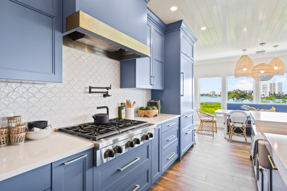Design ideas for a mid-sized beach style l-shaped open plan kitchen in Other with a farmhouse sink, shaker cabinets, blue cabinets, quartz benchtops, white splashback, porcelain splashback, black appliances, porcelain floors, with island, brown floor, white benchtop and timber.