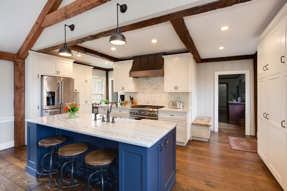 This is an example of a mid-sized country l-shaped open plan kitchen in Providence with a farmhouse sink, beaded inset cabinets, white cabinets, quartzite benchtops, white splashback, brick splashback, stainless steel appliances, medium hardwood floors and with island.
