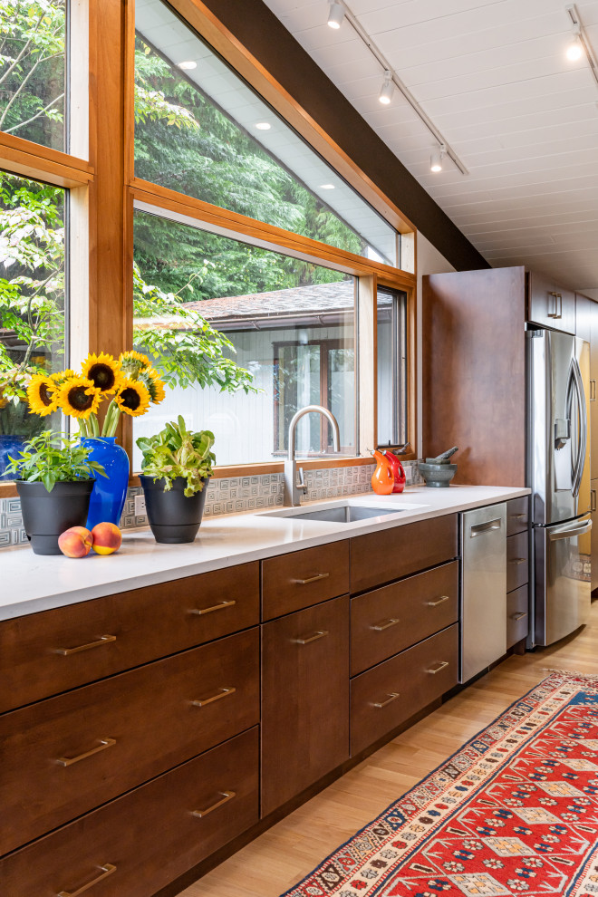 This is an example of a mid-sized midcentury open plan kitchen in Other with an undermount sink, flat-panel cabinets, brown cabinets, quartz benchtops, green splashback, mosaic tile splashback, stainless steel appliances, light hardwood floors, with island, beige floor, white benchtop and exposed beam.