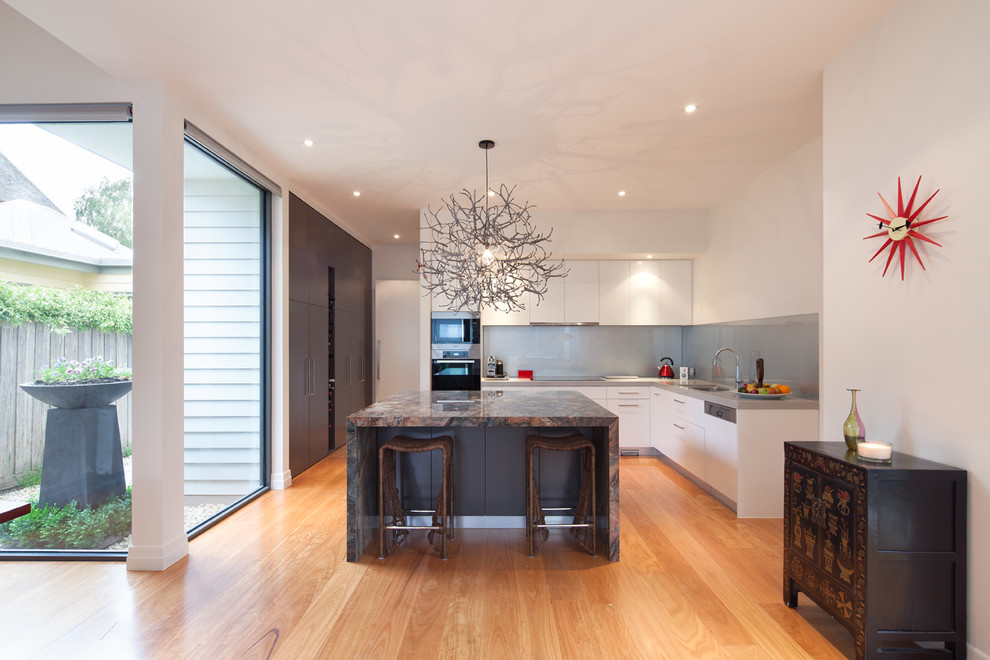 This is an example of a mid-sized contemporary l-shaped kitchen in Melbourne with an undermount sink, flat-panel cabinets, white cabinets, grey splashback, glass sheet splashback, light hardwood floors and with island.