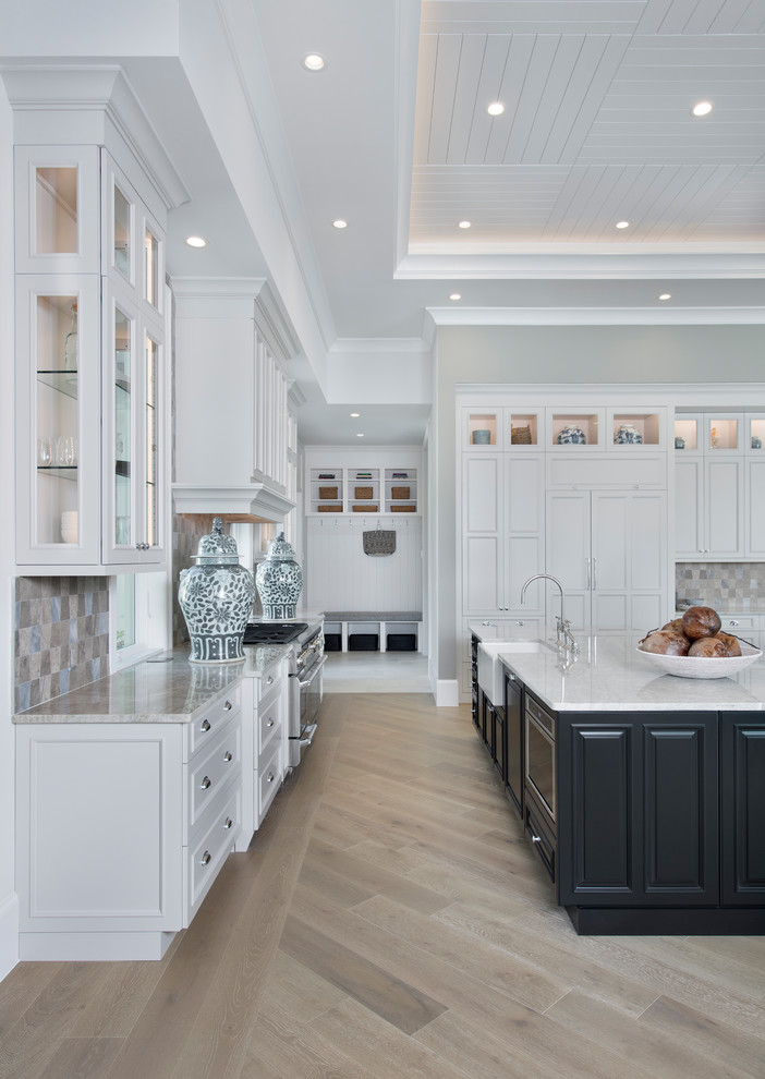 This is an example of a large transitional l-shaped open plan kitchen in Miami with a farmhouse sink, recessed-panel cabinets, white cabinets, marble benchtops, grey splashback, ceramic splashback, panelled appliances, light hardwood floors and multiple islands.
