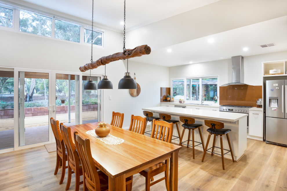 Photo of a large contemporary kitchen/dining combo in Perth with white walls, laminate floors, a two-sided fireplace, a stone fireplace surround, brown floor and vaulted.