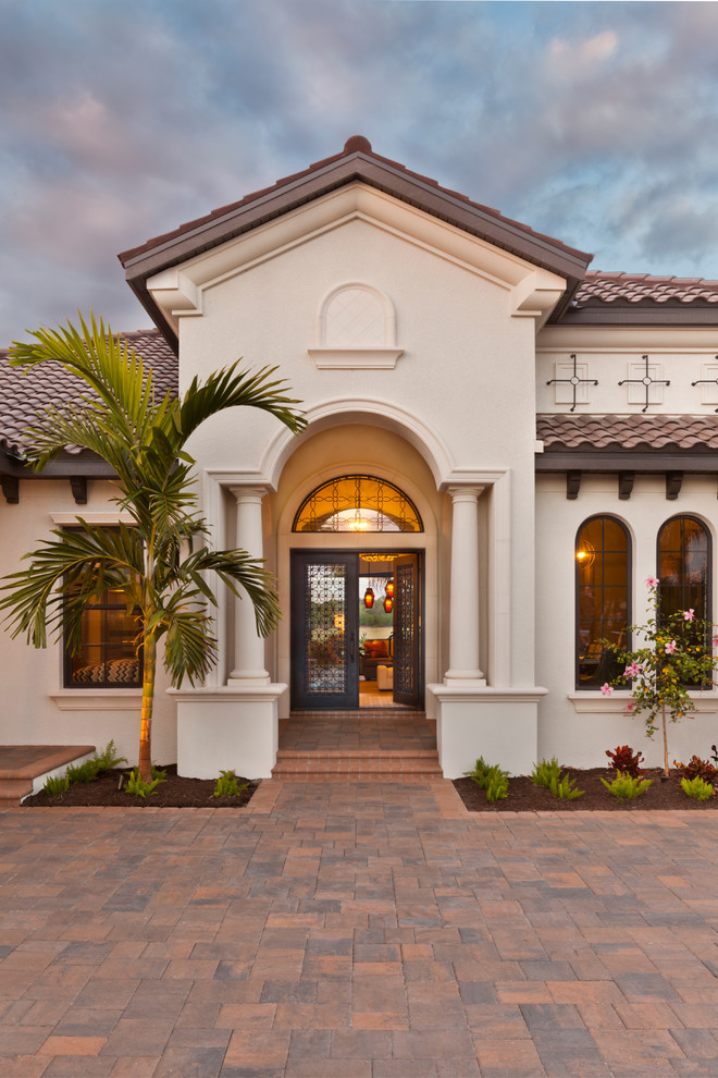 This is an example of an expansive mediterranean one-storey stucco white house exterior in Tampa with a hip roof and a shingle roof.