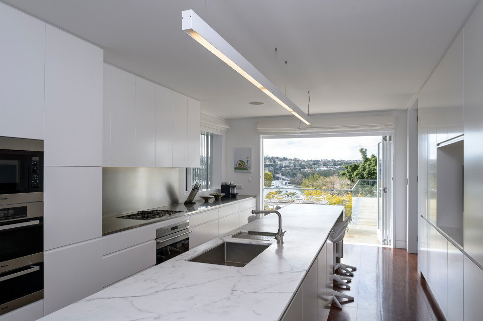 Inspiration for a contemporary galley kitchen in Sydney with an undermount sink, metallic splashback, stainless steel appliances, dark hardwood floors, with island, brown floor, white benchtop, flat-panel cabinets and white cabinets.
