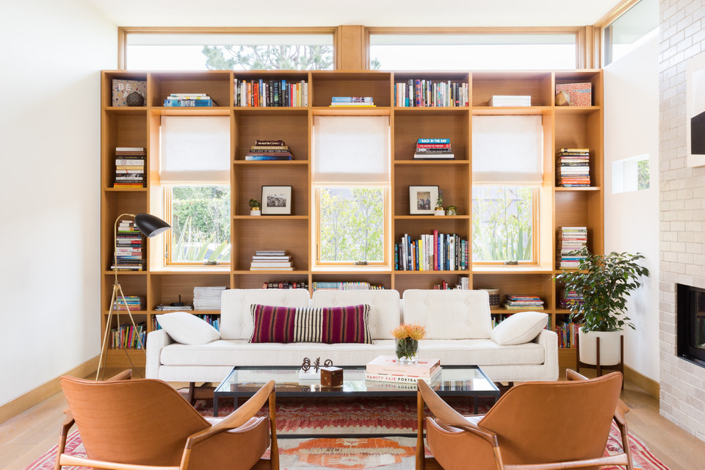 This is an example of a mid-sized contemporary open concept living room in Los Angeles with a library, white walls, medium hardwood floors, a standard fireplace, a brick fireplace surround and brown floor.