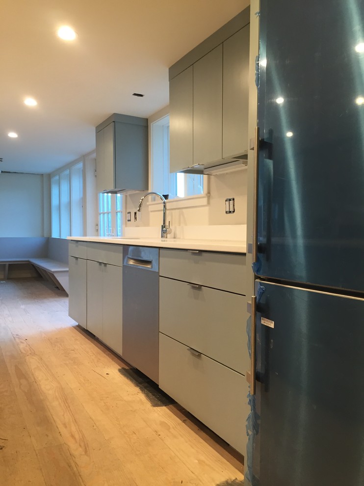 This is an example of a mid-sized modern galley eat-in kitchen in New York with an undermount sink, flat-panel cabinets, grey cabinets, quartz benchtops, white splashback, stone slab splashback, stainless steel appliances, painted wood floors, with island, black floor and white benchtop.