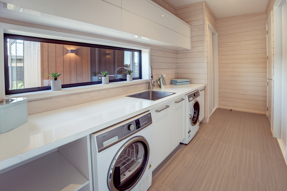 Photo of a large scandinavian galley utility room in Christchurch with a drop-in sink, white cabinets, laminate benchtops, white walls, ceramic floors, a side-by-side washer and dryer, grey floor and flat-panel cabinets.