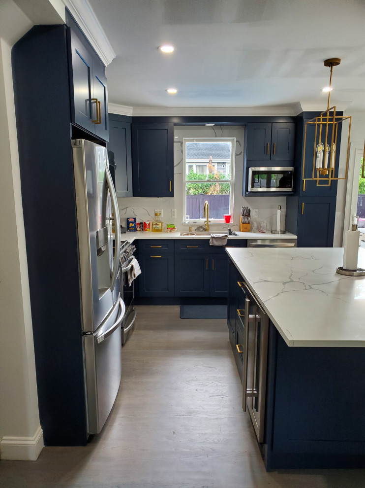 Modern inredning av ett mellanstort vit vitt kök, med en undermonterad diskho, skåp i shakerstil, blå skåp, bänkskiva i kvarts, vitt stänkskydd, rostfria vitvaror, mellanmörkt trägolv, en köksö och grått golv