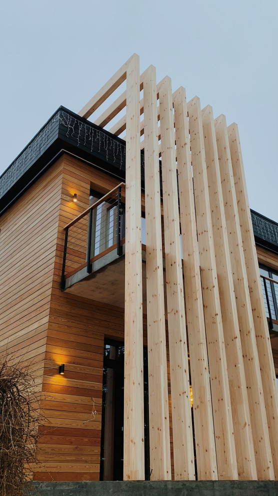 Foto della facciata di una casa grande beige contemporanea a tre piani con rivestimento in legno, tetto piano, copertura mista, tetto nero e pannelli sovrapposti