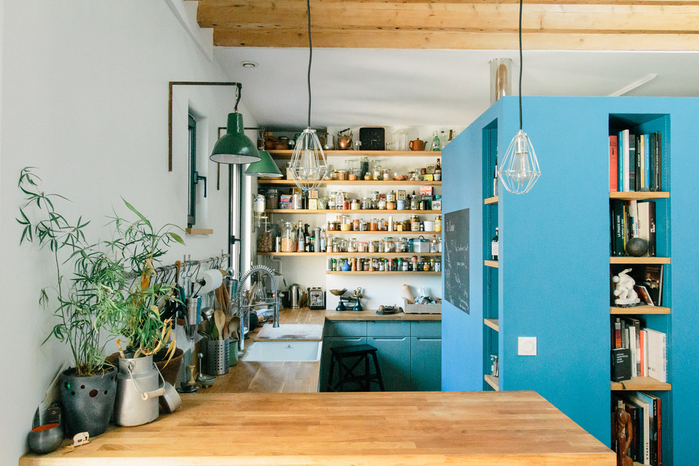 Photo of an industrial u-shaped kitchen in Paris with an undermount sink, flat-panel cabinets, turquoise cabinets, wood benchtops, white splashback, a peninsula and brown benchtop.