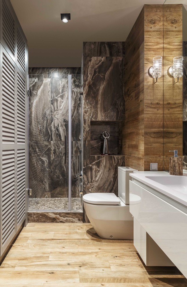 This is an example of a contemporary 3/4 bathroom in Moscow with flat-panel cabinets, white cabinets, a two-piece toilet, brown tile, an integrated sink, brown floor, white benchtops, a corner shower, grey walls and light hardwood floors.