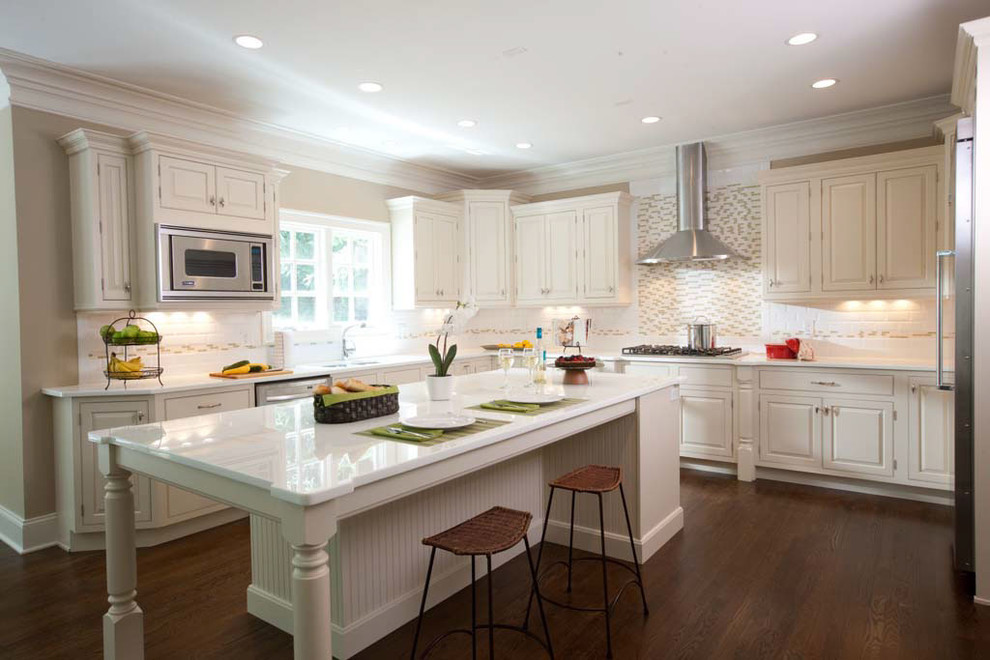 Large transitional l-shaped dark wood floor and brown floor eat-in kitchen photo with a drop-in sink, raised-panel cabinets, white cabinets, solid surface countertops, white backsplash, ceramic backsplash, stainless steel appliances and an island