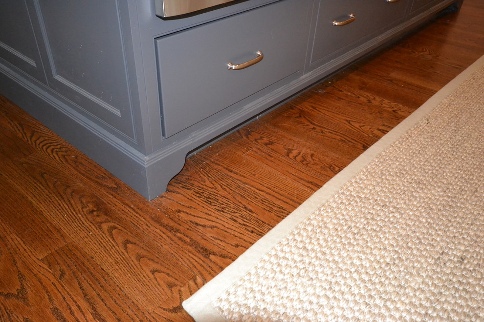 Example of a large transitional l-shaped medium tone wood floor kitchen pantry design in Philadelphia with an undermount sink, flat-panel cabinets, white cabinets, quartz countertops, white backsplash, stone tile backsplash, stainless steel appliances and an island