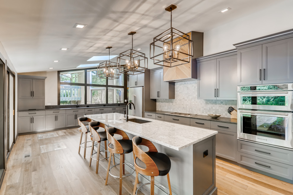 Transitional u-shaped medium tone wood floor, brown floor and vaulted ceiling kitchen photo in Chicago with an undermount sink, recessed-panel cabinets, gray cabinets, gray backsplash, stainless steel appliances, an island and multicolored countertops