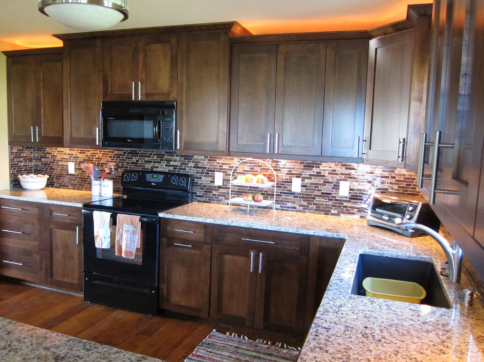Photo of a large traditional u-shaped open plan kitchen in Milwaukee with an undermount sink, shaker cabinets, dark wood cabinets, granite benchtops, multi-coloured splashback, black appliances and medium hardwood floors.