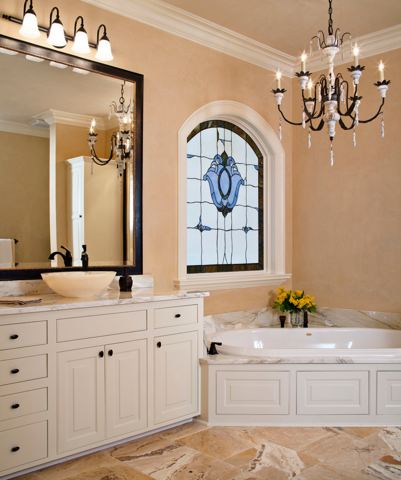 Photo of a large traditional master bathroom in New Orleans with a vessel sink, beaded inset cabinets, white cabinets, marble benchtops, a corner tub, a corner shower, beige tile, stone tile, beige walls and marble floors.
