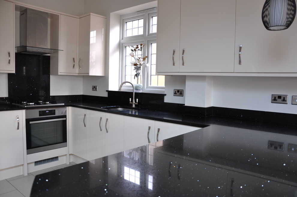 This is an example of a mid-sized contemporary u-shaped eat-in kitchen in London with a single-bowl sink, flat-panel cabinets, beige cabinets, quartzite benchtops, black splashback, stone slab splashback, stainless steel appliances, porcelain floors, a peninsula, grey floor and black benchtop.