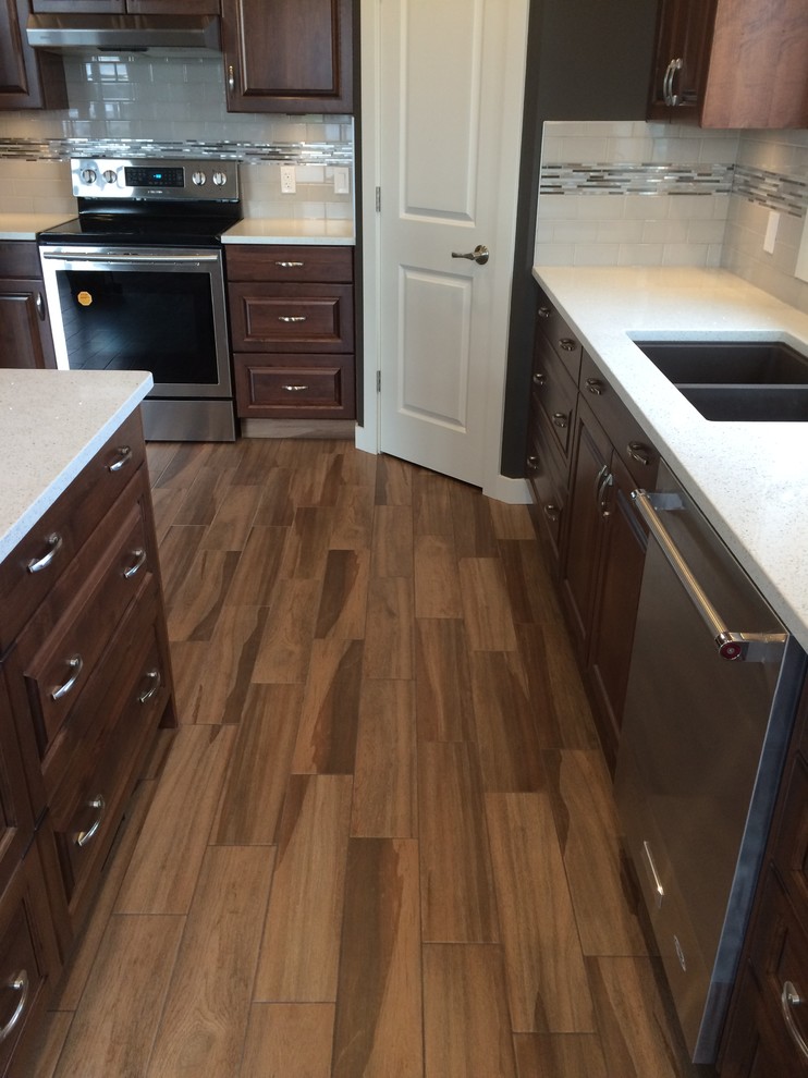 Eat-in kitchen - mid-sized transitional u-shaped porcelain tile and brown floor eat-in kitchen idea in Edmonton with a double-bowl sink, raised-panel cabinets, brown cabinets, quartzite countertops, white backsplash, ceramic backsplash, stainless steel appliances and an island