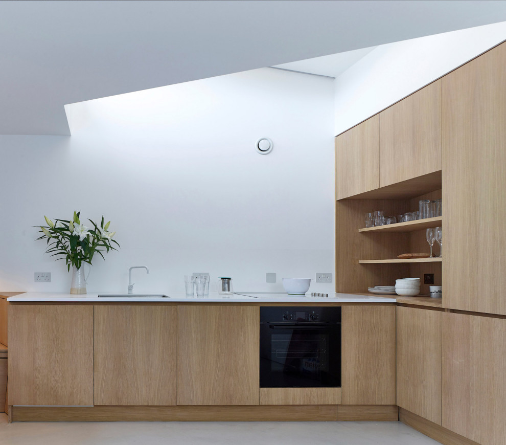 Mid-sized contemporary l-shaped kitchen in London with an undermount sink, flat-panel cabinets, light wood cabinets, panelled appliances, grey floor and white benchtop.