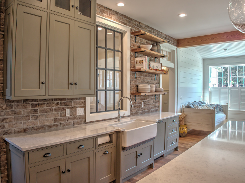 Inspiration for a mid-sized transitional l-shaped open plan kitchen in Philadelphia with a farmhouse sink, shaker cabinets, grey cabinets, quartz benchtops, red splashback, brick splashback, stainless steel appliances, light hardwood floors, with island, beige floor and white benchtop.
