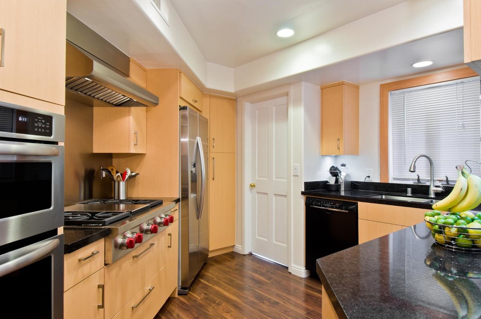 Small trendy u-shaped medium tone wood floor eat-in kitchen photo with flat-panel cabinets, a double-bowl sink, light wood cabinets, granite countertops, stainless steel appliances and white walls