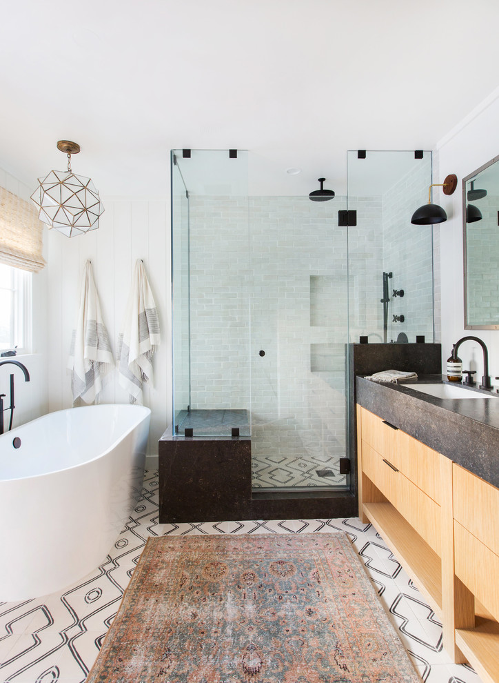 This is an example of a beach style master bathroom in San Diego with flat-panel cabinets, medium wood cabinets, a freestanding tub, a corner shower, white tile, white walls, an undermount sink, white floor, a hinged shower door and black benchtops.