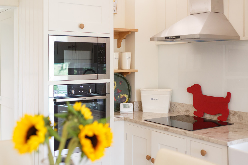 Design ideas for a medium sized bohemian l-shaped kitchen/diner with a belfast sink, shaker cabinets, white cabinets, granite worktops, metallic splashback, mirror splashback, black appliances, porcelain flooring and grey floors.