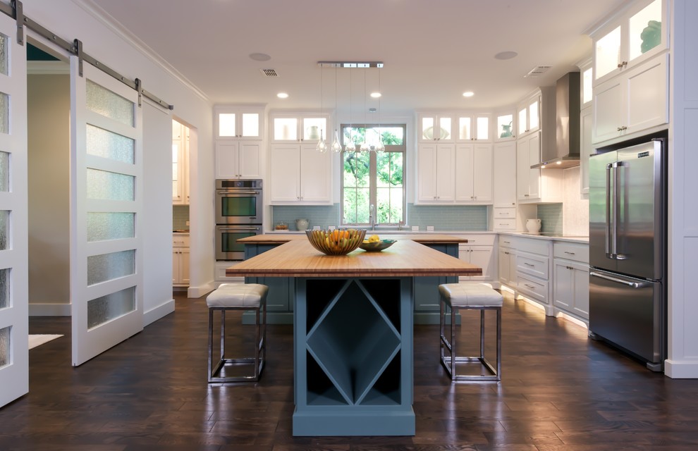 This is an example of a large contemporary l-shaped open plan kitchen in Dallas with a farmhouse sink, shaker cabinets, white cabinets, blue splashback, glass tile splashback, stainless steel appliances, dark hardwood floors, multiple islands and wood benchtops.