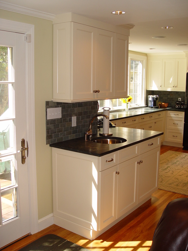 Example of a transitional kitchen design in Boston with an undermount sink, recessed-panel cabinets, white cabinets, granite countertops, black appliances and an island