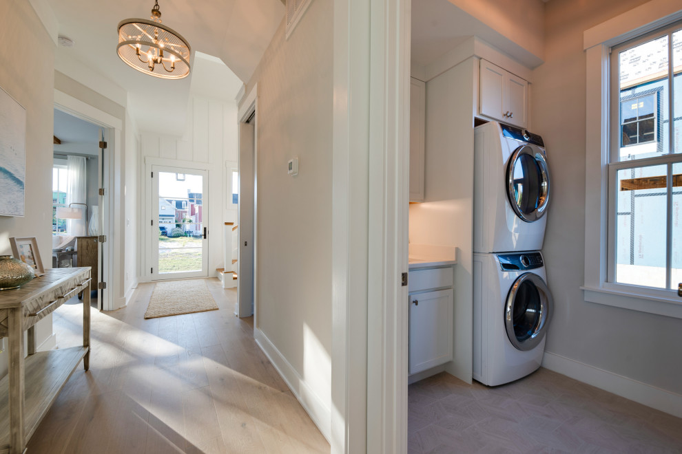 Photo of a small country single-wall dedicated laundry room in Other with an undermount sink, shaker cabinets, white cabinets, quartz benchtops, white splashback, marble splashback, porcelain floors, a stacked washer and dryer, grey floor and white benchtop.