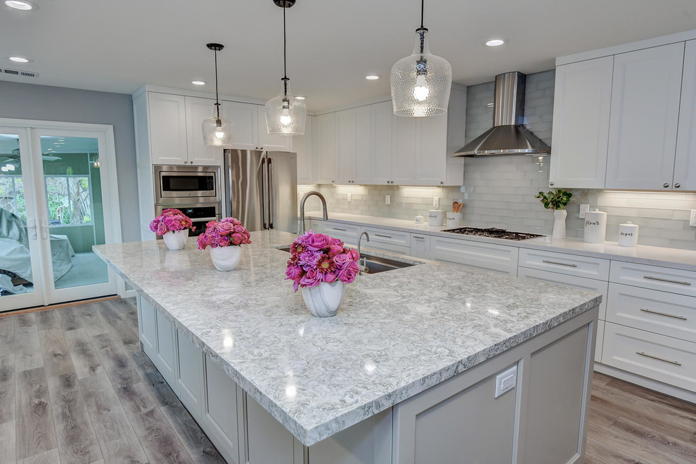 This is an example of a large contemporary open plan kitchen in San Francisco with a single-bowl sink, raised-panel cabinets, white cabinets, quartzite benchtops, grey splashback, porcelain splashback, stainless steel appliances, ceramic floors, with island, grey floor and grey benchtop.