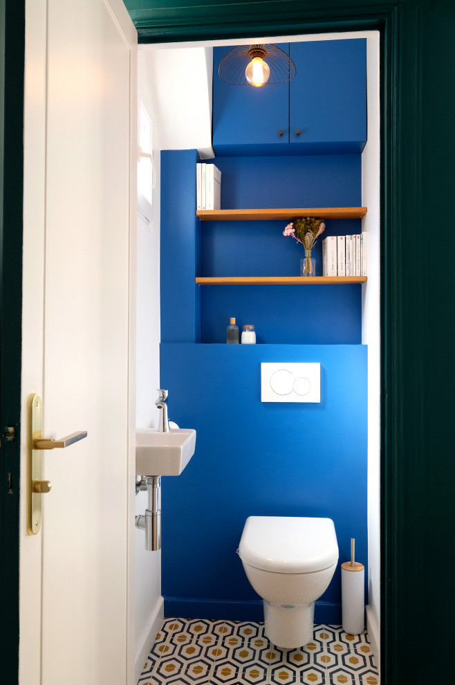 Inspiration for a small modern powder room in Paris with beaded inset cabinets, blue cabinets, a wall-mount toilet, blue tile, blue walls, cement tiles, a wall-mount sink, yellow floor and a built-in vanity.