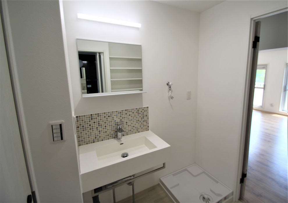 Foto på ett rustikt vit toalett, med öppna hyllor, vita skåp, brun kakel, mosaik, vita väggar, vinylgolv, ett väggmonterat handfat, bänkskiva i akrylsten och grått golv