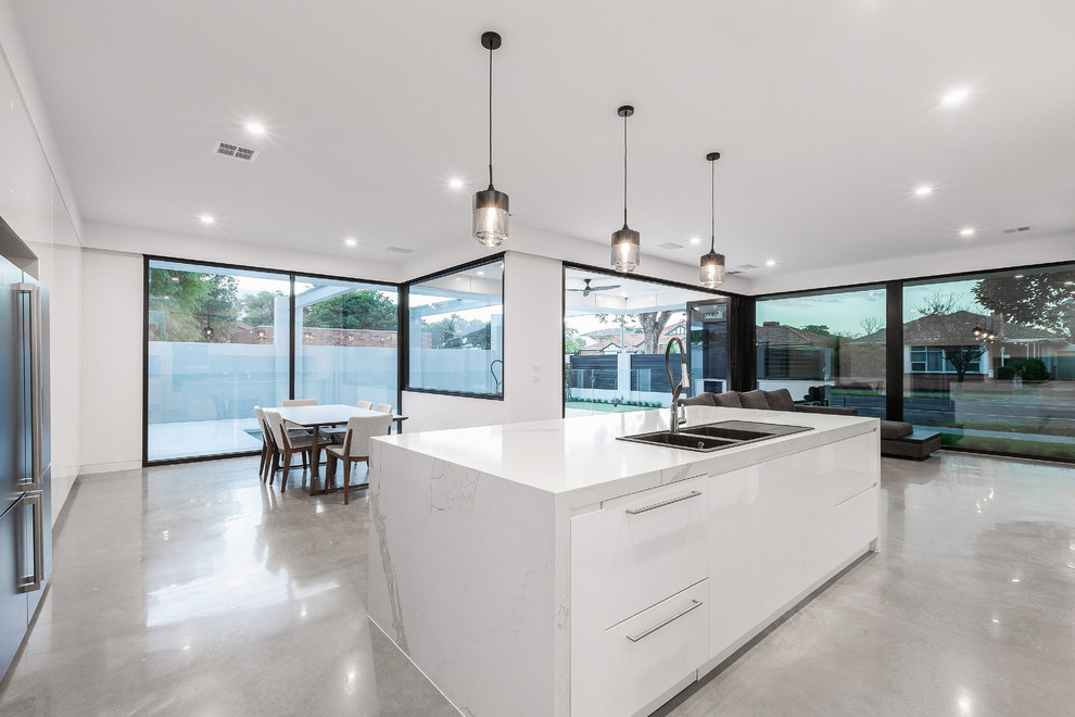 This is an example of a mid-sized contemporary l-shaped open plan kitchen in Melbourne with white cabinets, marble benchtops, mirror splashback, black appliances, concrete floors, with island, grey floor and white benchtop.
