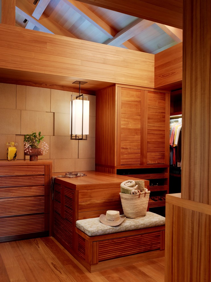 Photo of a tropical gender-neutral walk-in wardrobe in Hawaii with louvered cabinets, medium wood cabinets, medium hardwood floors and brown floor.