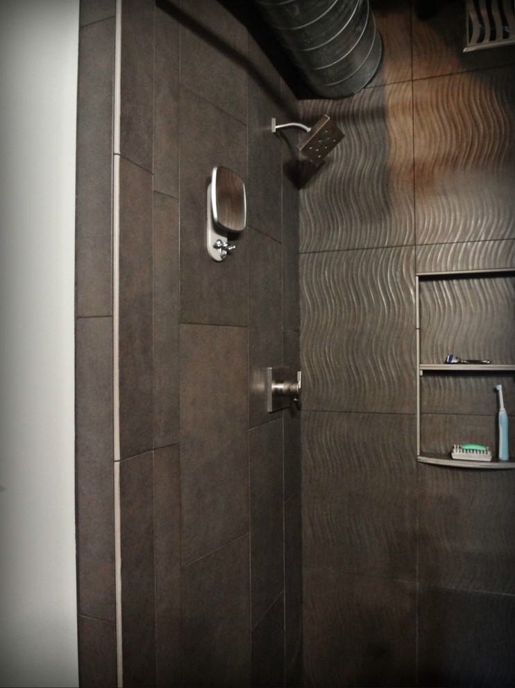 Photo of a mid-sized industrial master bathroom in Portland with an integrated sink, a drop-in tub, an open shower, a one-piece toilet, gray tile, porcelain tile, grey walls, concrete floors, flat-panel cabinets, black cabinets and stainless steel benchtops.