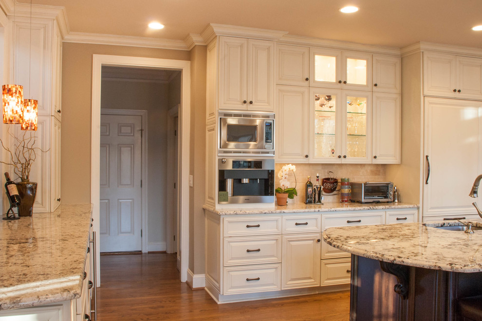 Design ideas for a mid-sized transitional u-shaped open plan kitchen in Raleigh with an undermount sink, raised-panel cabinets, white cabinets, granite benchtops, beige splashback, subway tile splashback, stainless steel appliances, medium hardwood floors and with island.