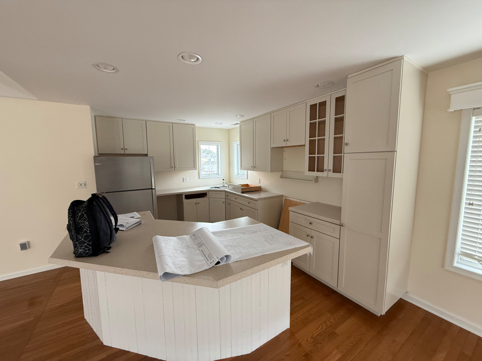 Example of a large beach style u-shaped medium tone wood floor eat-in kitchen design with shaker cabinets, white cabinets, laminate countertops, an island and beige countertops