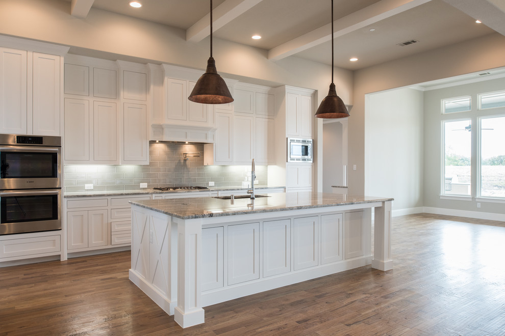 Eat-in kitchen - large transitional u-shaped medium tone wood floor and brown floor eat-in kitchen idea in Dallas with a drop-in sink, recessed-panel cabinets, white cabinets, granite countertops, beige backsplash, ceramic backsplash, stainless steel appliances, an island and multicolored countertops
