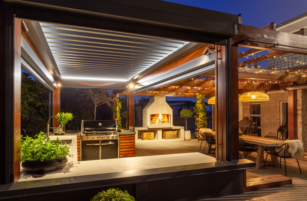 Photo of a mid-sized mediterranean courtyard patio in Other with an outdoor kitchen, natural stone pavers and a pergola.